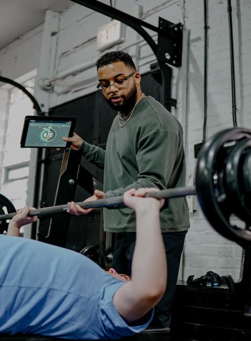 Falcon trainer coaching a member through a tracked bench press